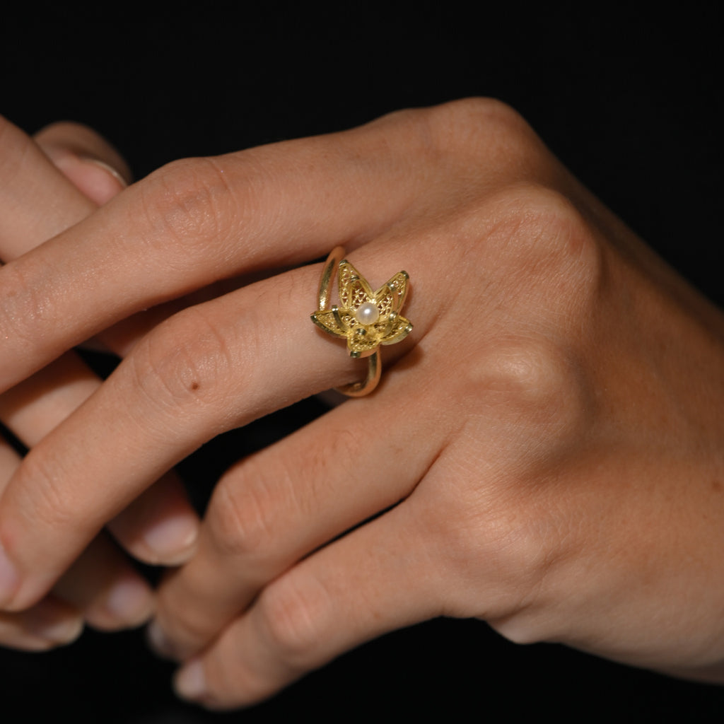 Close-up of a hand wearing a gold ring with a butterfly design on a dark background