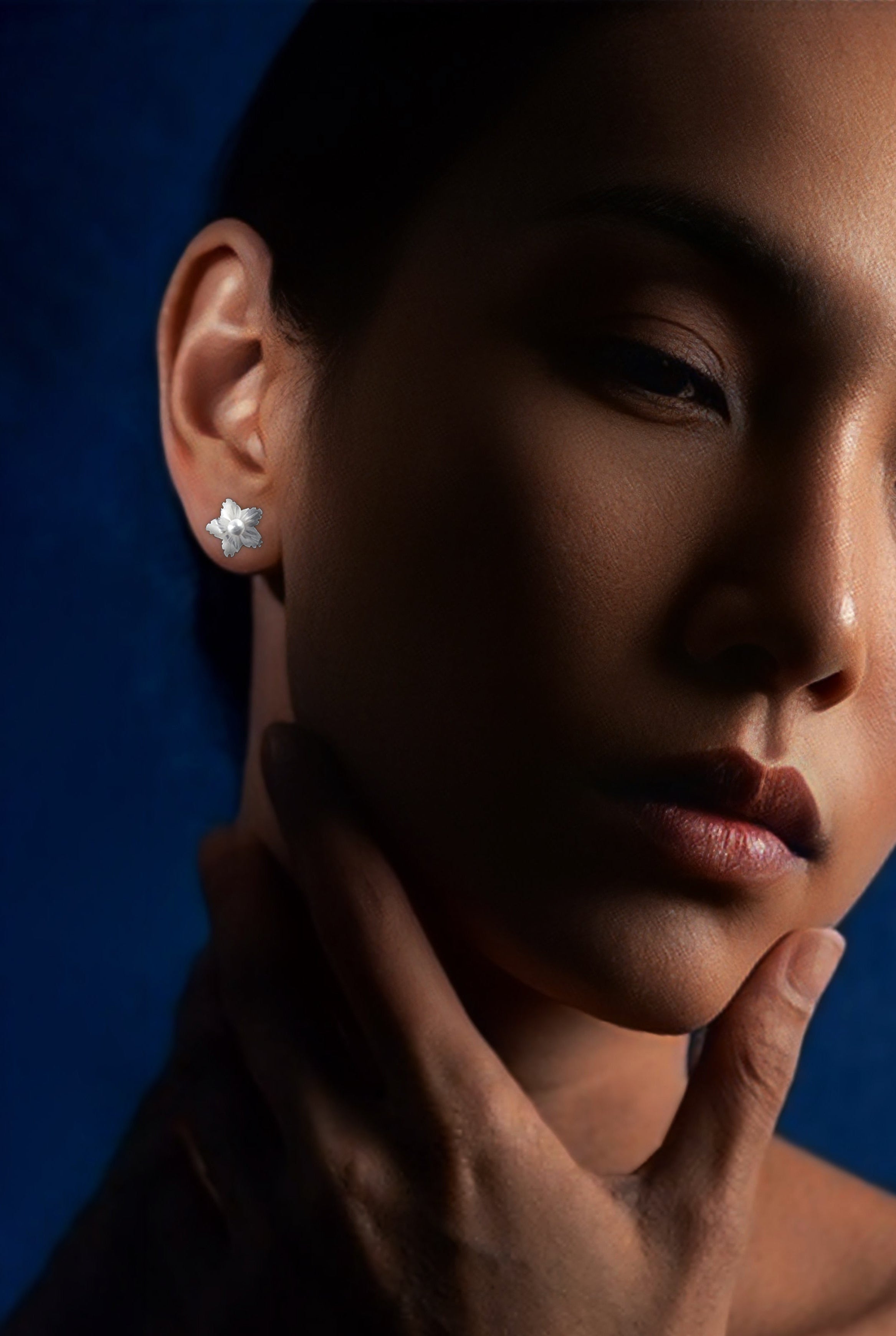Close-up of a person wearing a diamond earring against a blue background