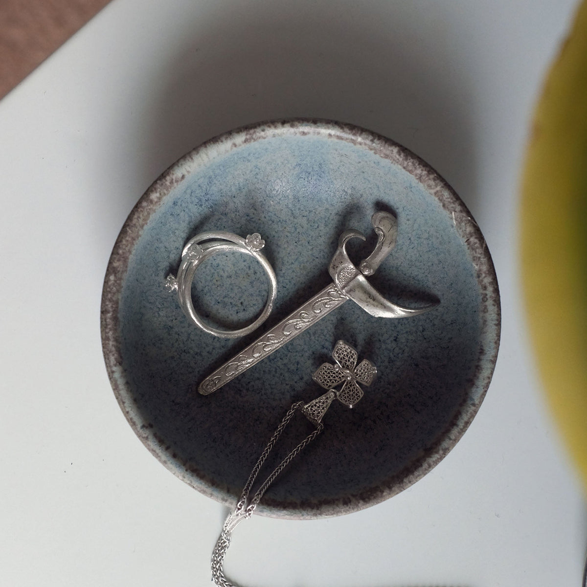 Silver pendant with floral design on a dark blue ceramic jewellery dish