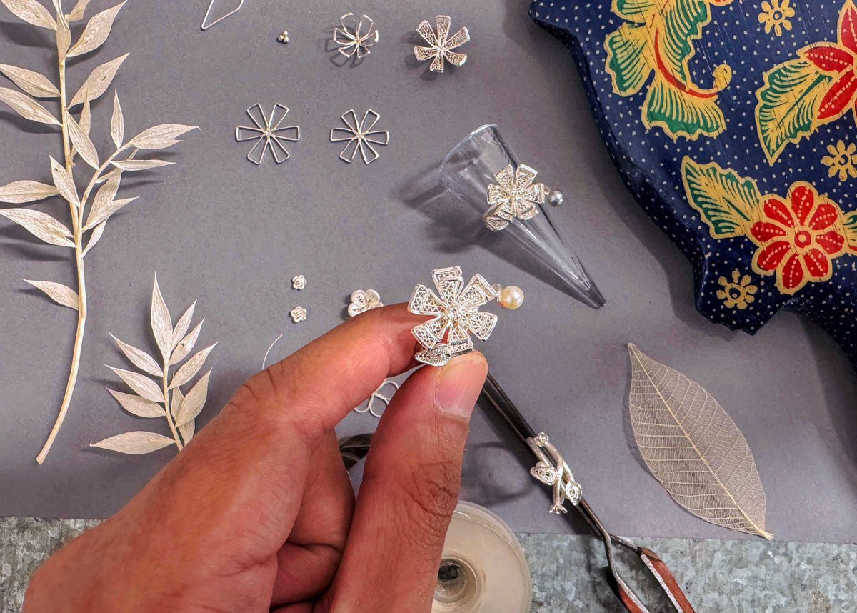 Hand holding a silver earring with floral design on a gray surface with decorative elements.