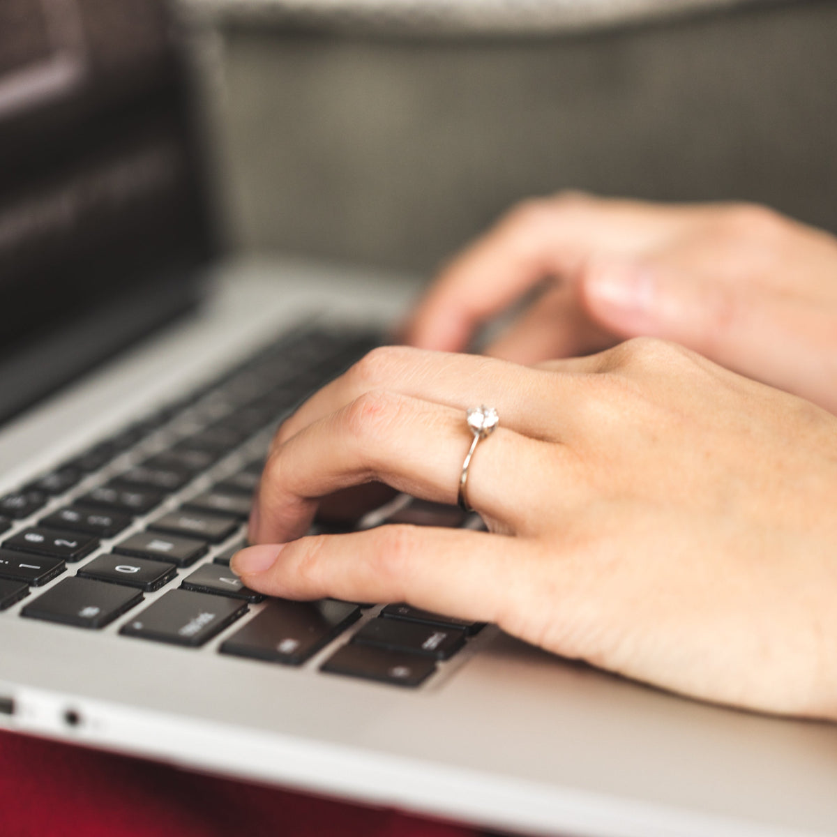Close-up of hands typing on a laptop keyboard with a ring on one finger.