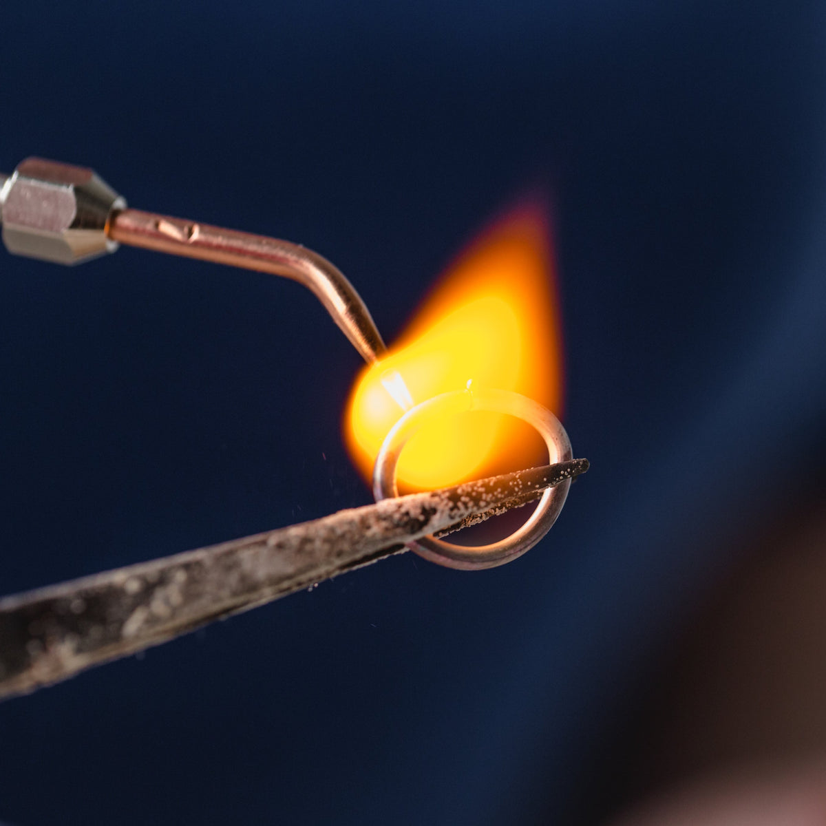 Close-up of a ring being heated by a torch flame against a dark background